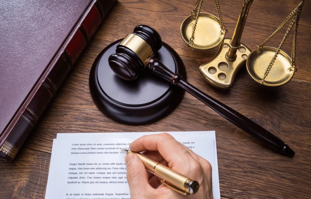 A man's hand writing on a paper with legal imagery on the table