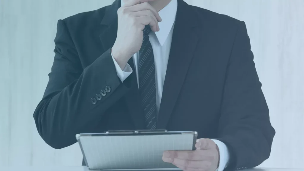 Whistleblower lawyer in a dark business suit holding a clipboard and resting a hand near their chin.