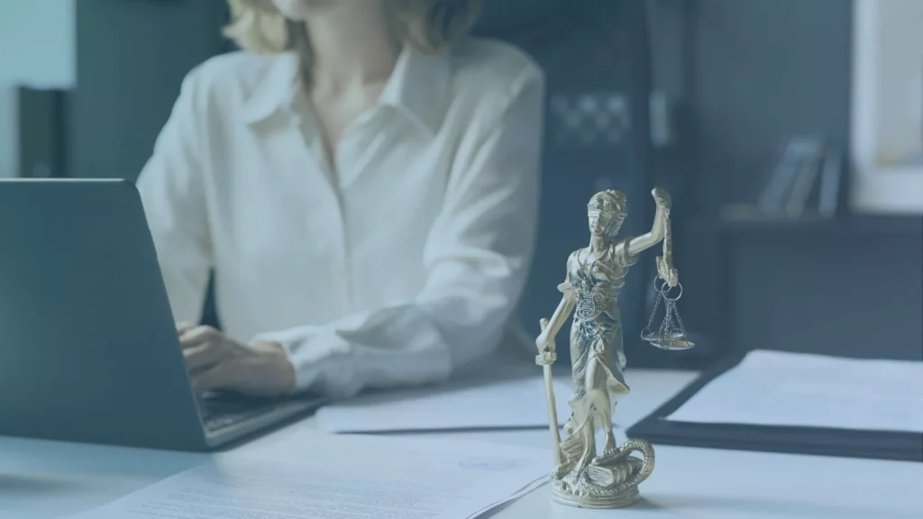 Person working on a laptop at a desk with a Lady Justice statue and unemployment representation documents in the foreground.