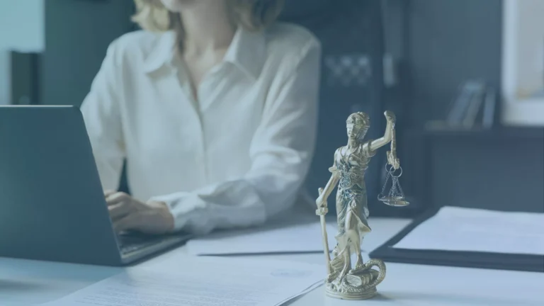 Person working on a laptop at a desk with a Lady Justice statue and unemployment representation documents in the foreground.