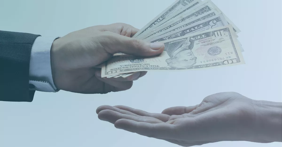 Close-up of one person handing cash to another person’s open hand.