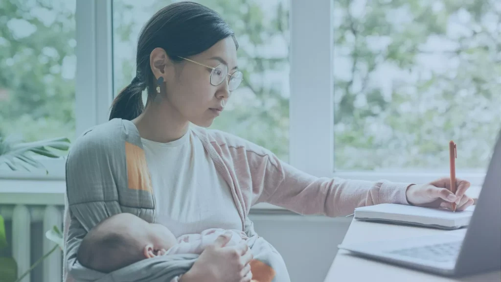 Mother working on a laptop while holding a baby, illustrating challenges of returning to work after a baby, and potential wrongful termination after maternity leave issues.