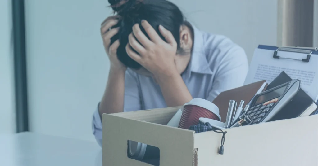 Employee sitting at a desk with a box of personal belongings after losing a job following medical leave.