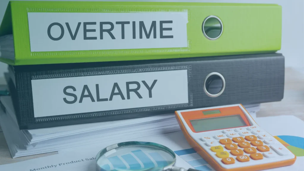 Office binders labeled "Overtime" and "Salary" beside a calculator, magnifying glass, and financial documents illustrating overtime pay and salaried employee wage compliance.